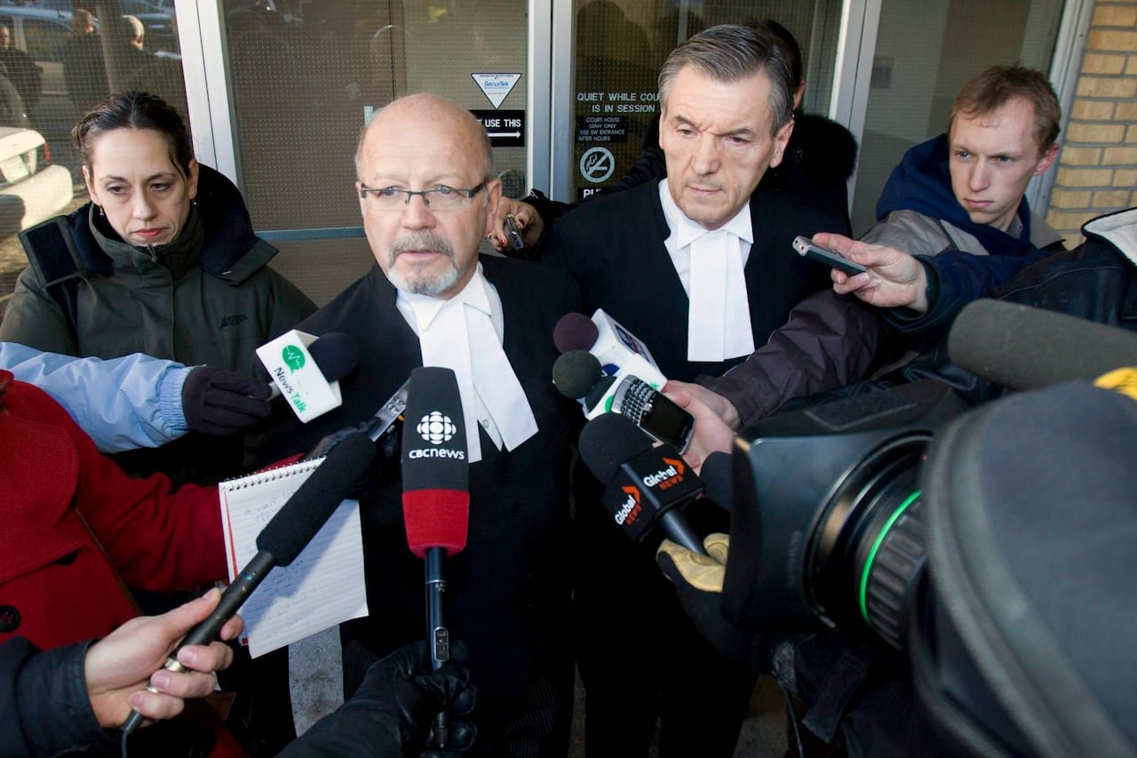 A crowd of people with microphones surround two men in black robes with white collars.